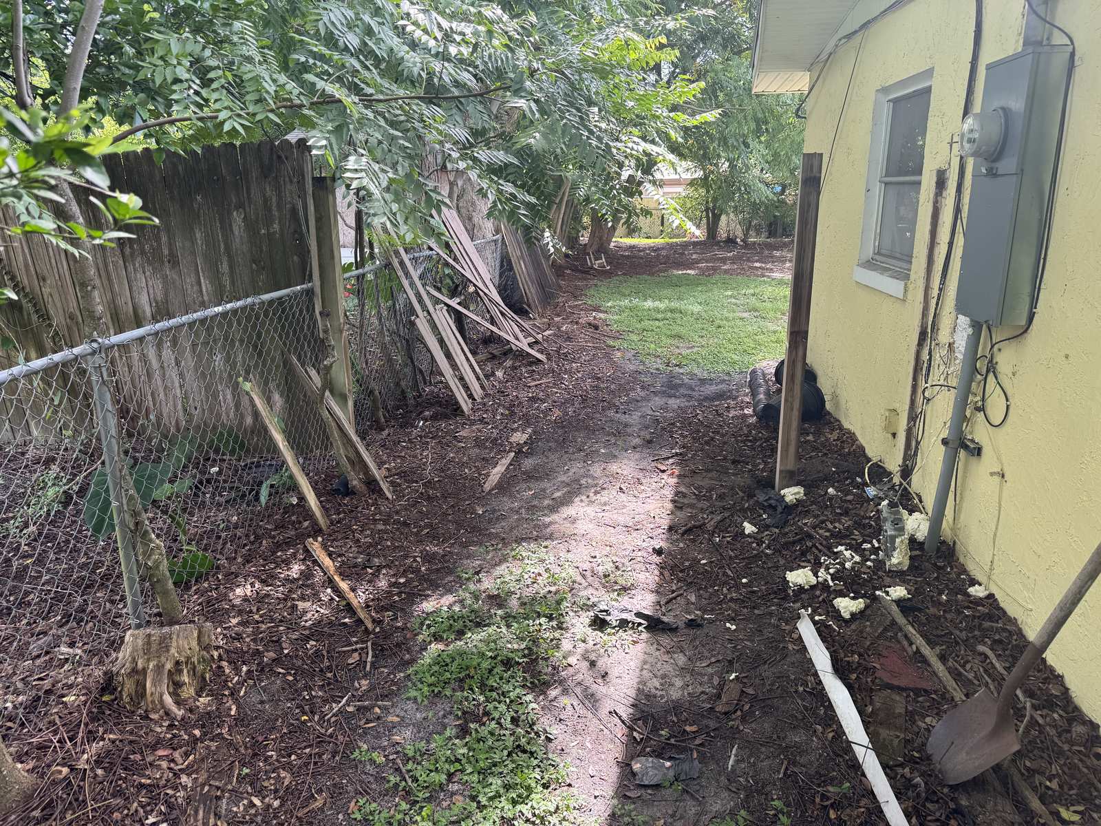 Side yard before the job: old wood fence panels down and stacked along the property line